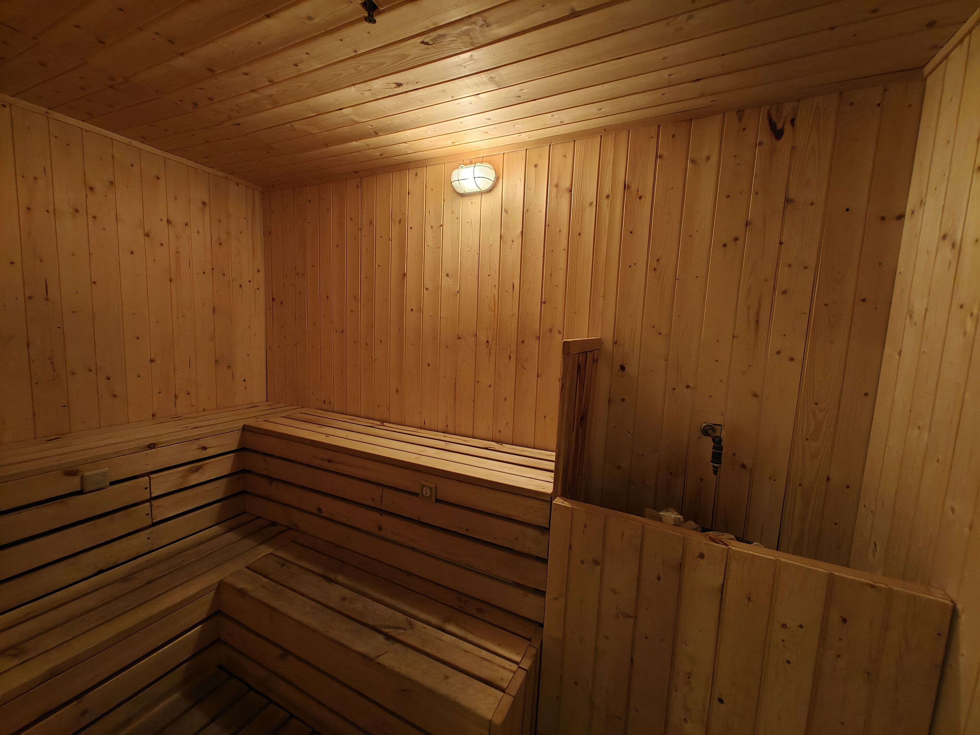 A wooden sauna with benches and a wall-mounted light fixture.