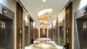 A modern hotel lobby with marble floors, wooden paneling, and a central light fixture.