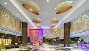 A modern hotel lobby with a reception desk, seating area, and decorative ceiling lights.