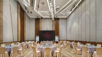 Un salón de conferencias en Crowne Plaza Guangzhou City Centre con mesas redondas, sillas y una pantalla grande al frente.