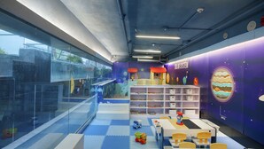A children's play area with a blue floor, tables, chairs, and a bookshelf.