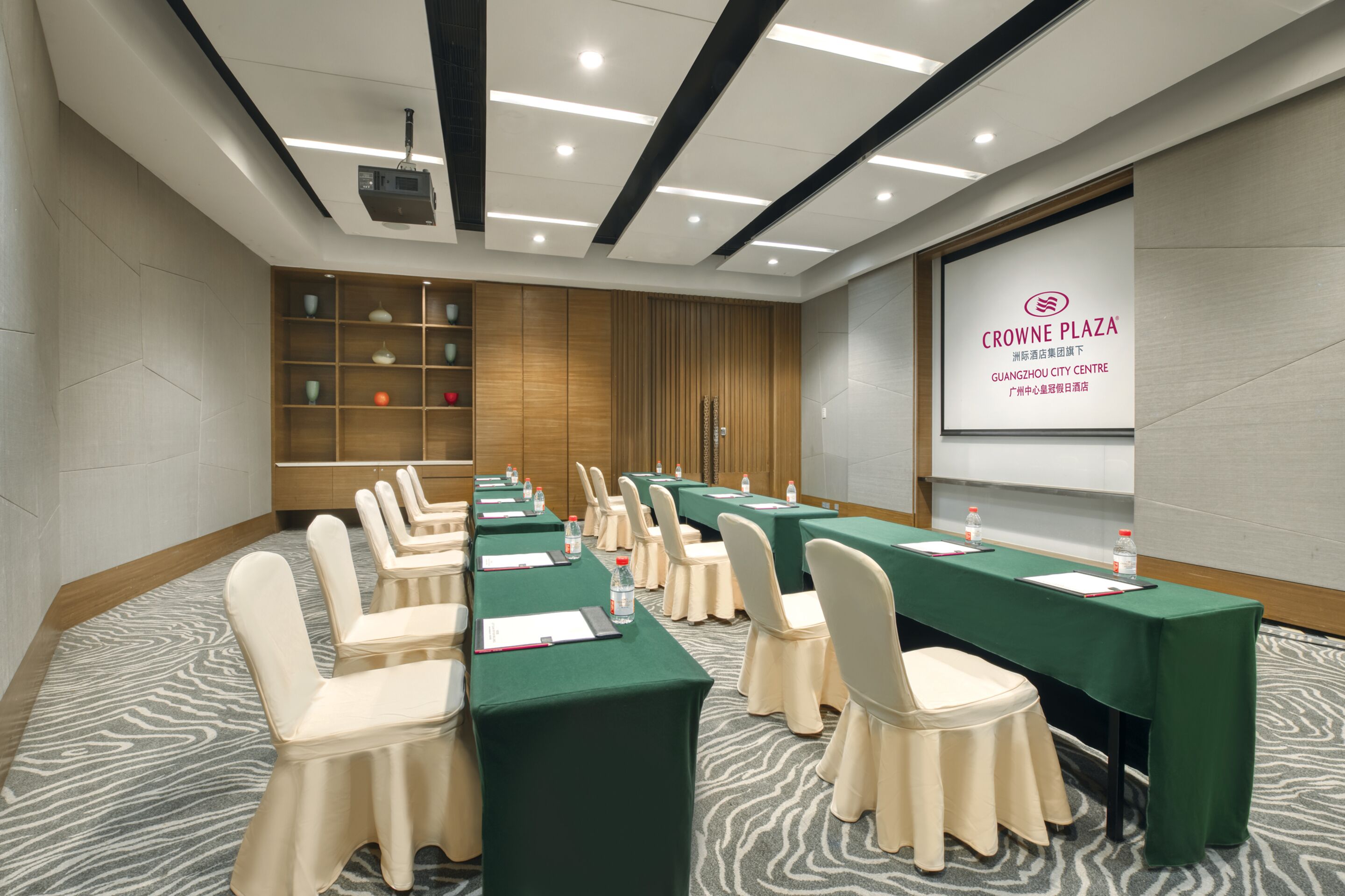A conference room with multiple tables and chairs, a projector screen, and a presentation on the wall.