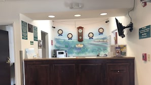 A reception desk with clocks, a landscape mural, and signs indicating room locations. - Sleep Inn Louisville Airport (Louisville)