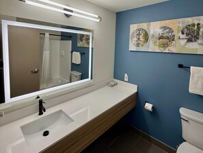 Un baño moderno con un espejo grande, un lavamanos, un inodoro y una pared de acento azul.