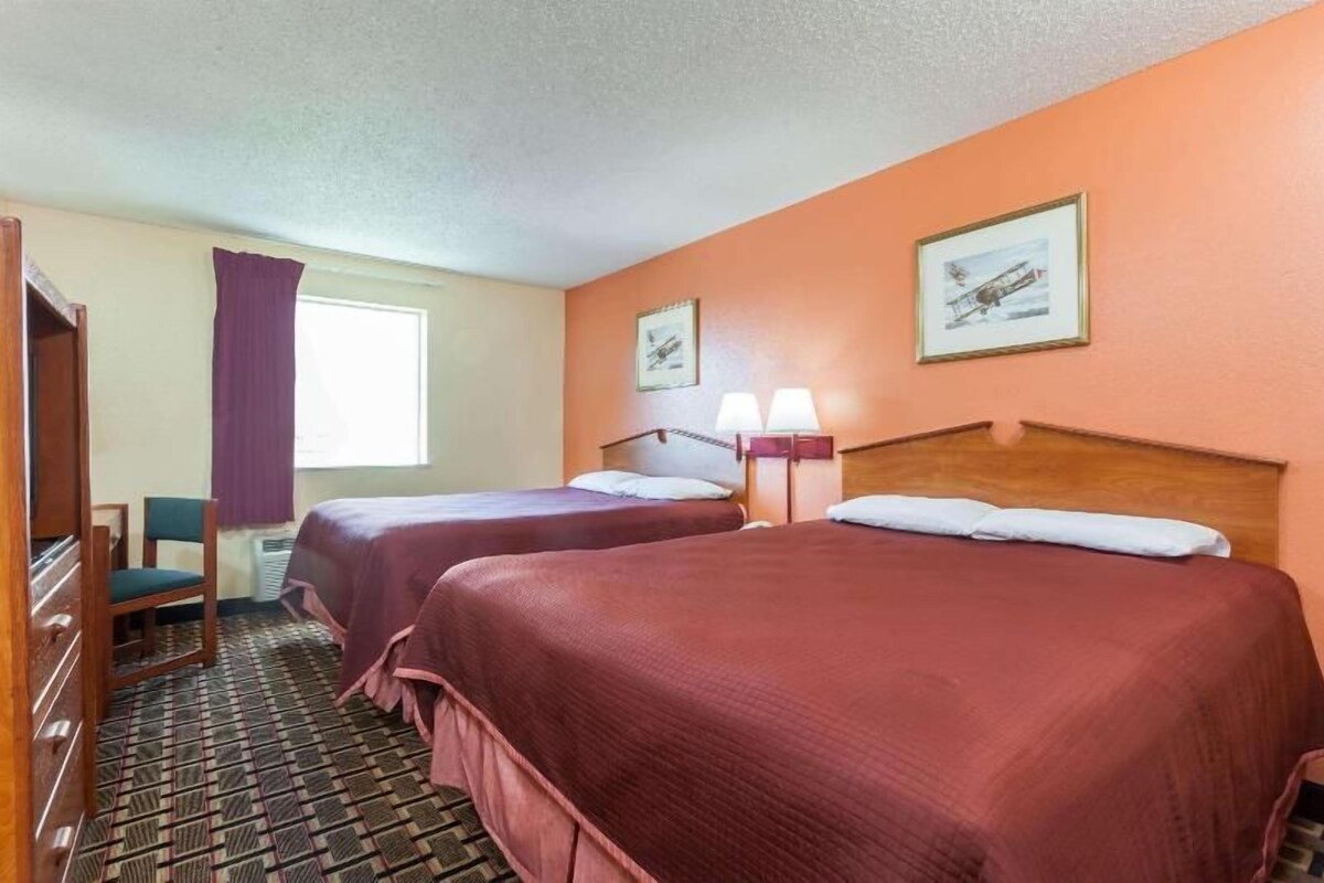 Una habitación de hotel con dos camas, un escritorio, una silla y una ventana con cortinas.