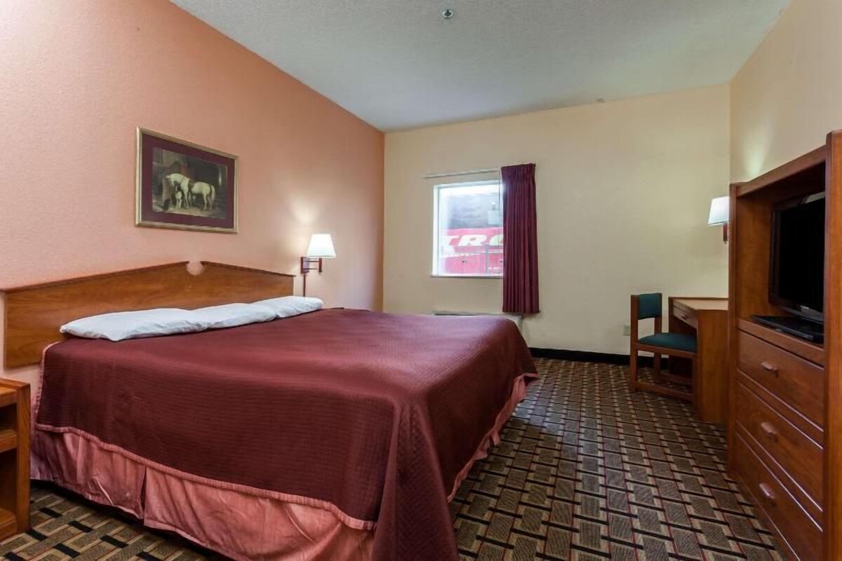 Una habitación de hotel con cama, escritorio, televisor y ventana con cortinas.