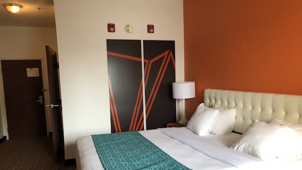 A hotel room with a bed, a nightstand, a lamp, and a door. - Sleep Inn Louisville Airport (Louisville)