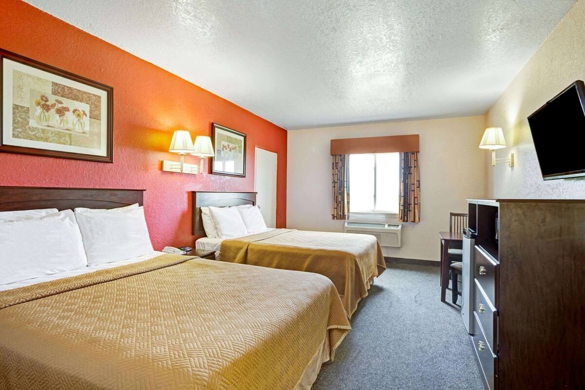 Habitación de hotel con dos camas, televisión, escritorio y ventana con cortinas.
