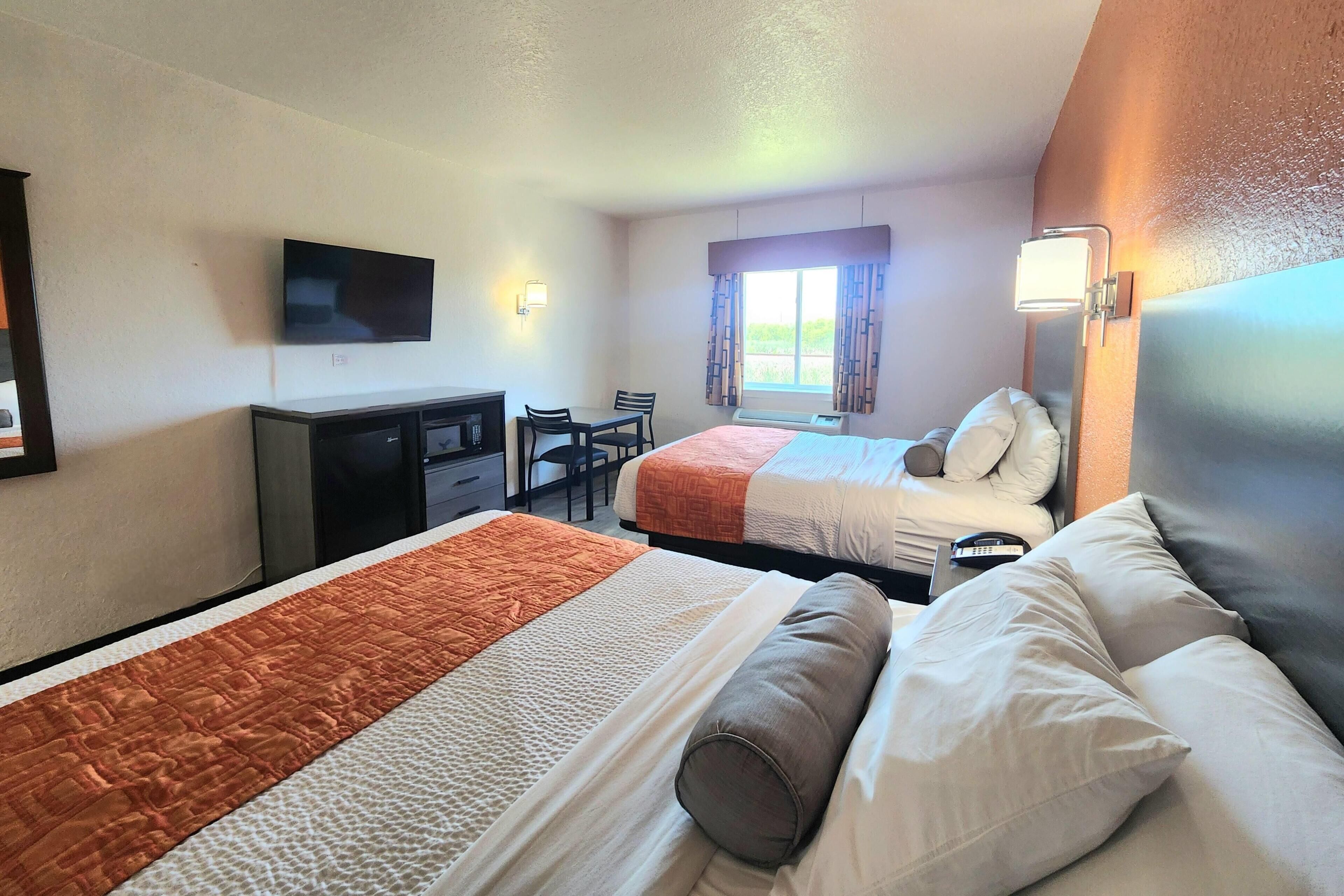 Habitación de hotel con dos camas, un escritorio, un televisor y una ventana con cortinas.