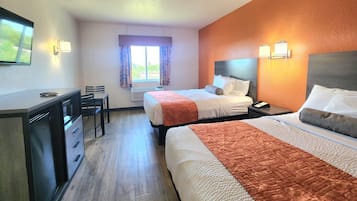 A hotel room with two beds, a desk, chairs, a window with curtains, and wall-mounted lights.
