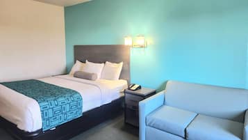 A hotel room with a bed, bedside table with a phone, and a chair.