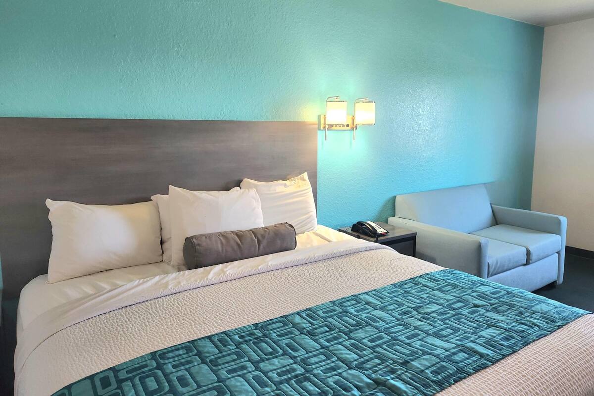 Una habitación de hotel con una cama, una silla y una mesita de noche con teléfono.