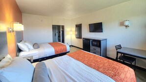 Una habitación de hotel con dos camas, un escritorio, una silla, un televisor y una lámpara de escritorio.
