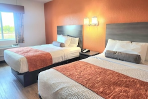 A hotel room with two beds, a window with curtains, a wall-mounted phone, and a light fixture.