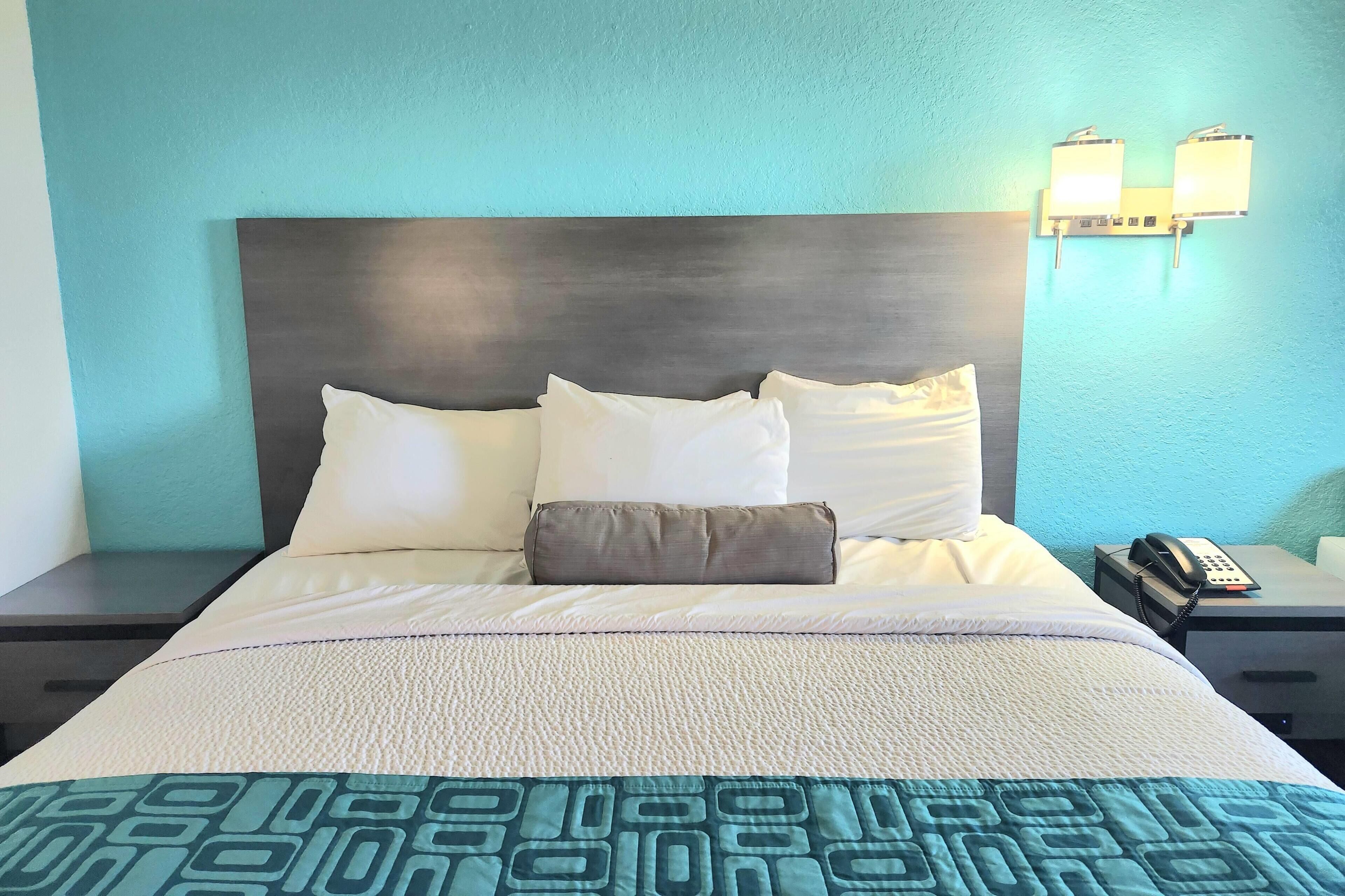 Una habitación de hotel con cama, mesita de noche, teléfono e iluminación en la pared.