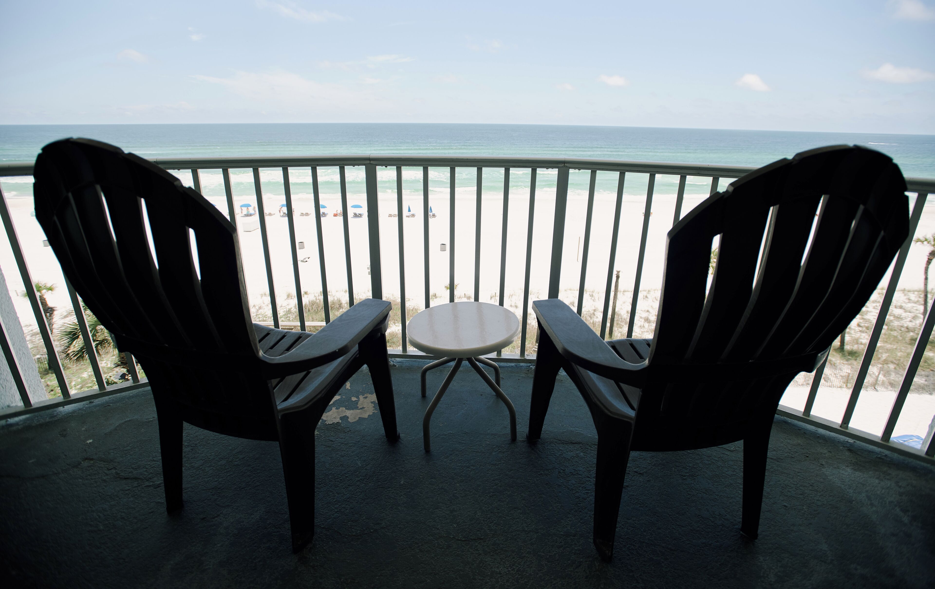 Two chairs and a small table on a balcony with a view of the beach and ocean.