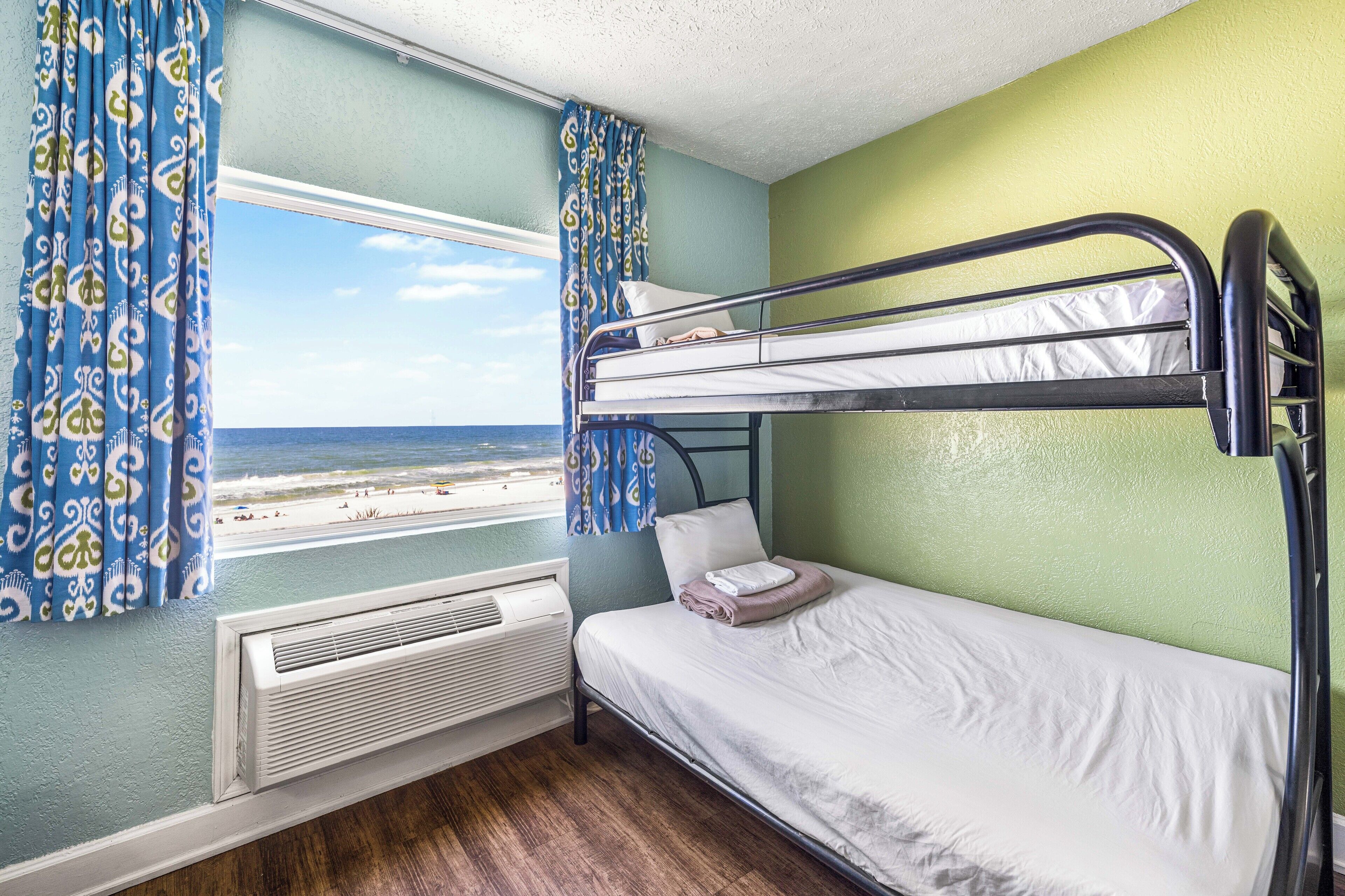 Een slaapkamer met stapelbed en uitzicht op een strand, een radiator en behang met patroon.