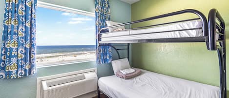 Een slaapkamer met stapelbed en uitzicht op een strand, een radiator en behang met patroon.
