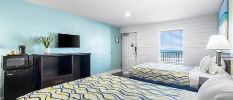 A hotel room with two beds, a TV, a desk with a lamp, a plant, and a window with blinds.