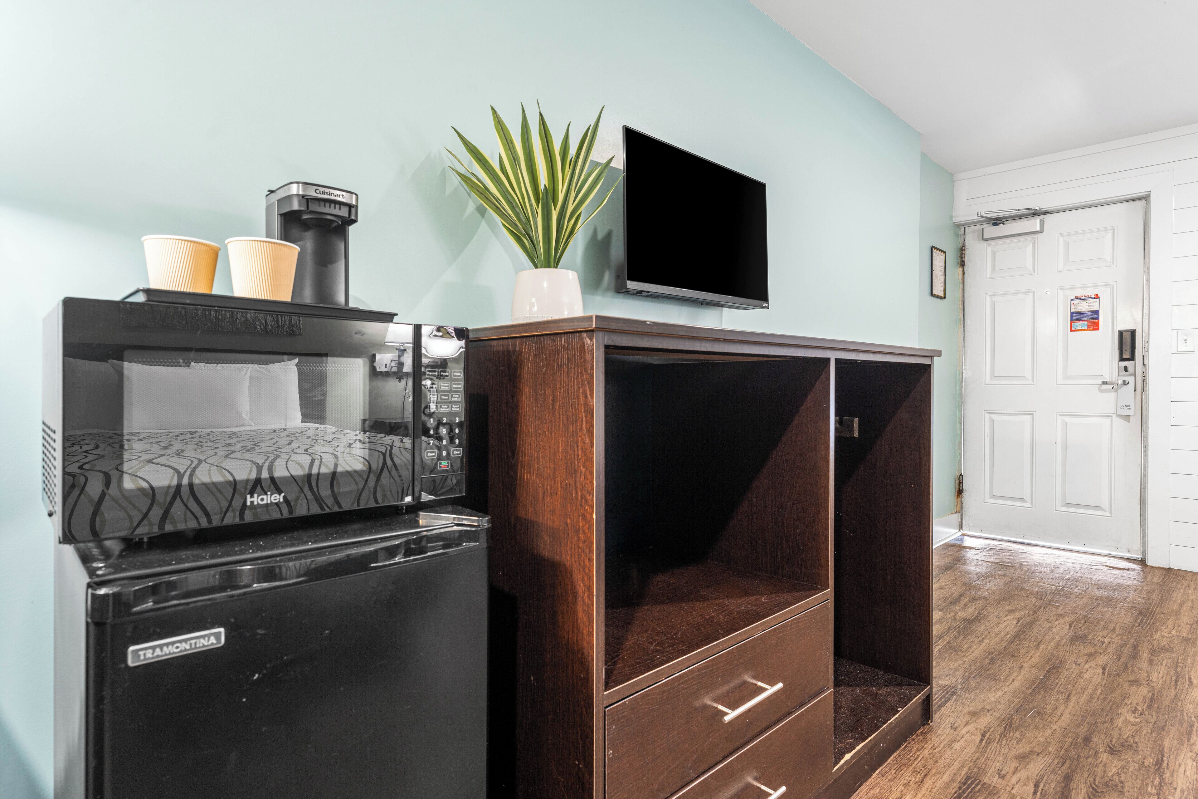 A kitchenette with a coffee maker, a refrigerator, and a flat-screen TV mounted on the wall.