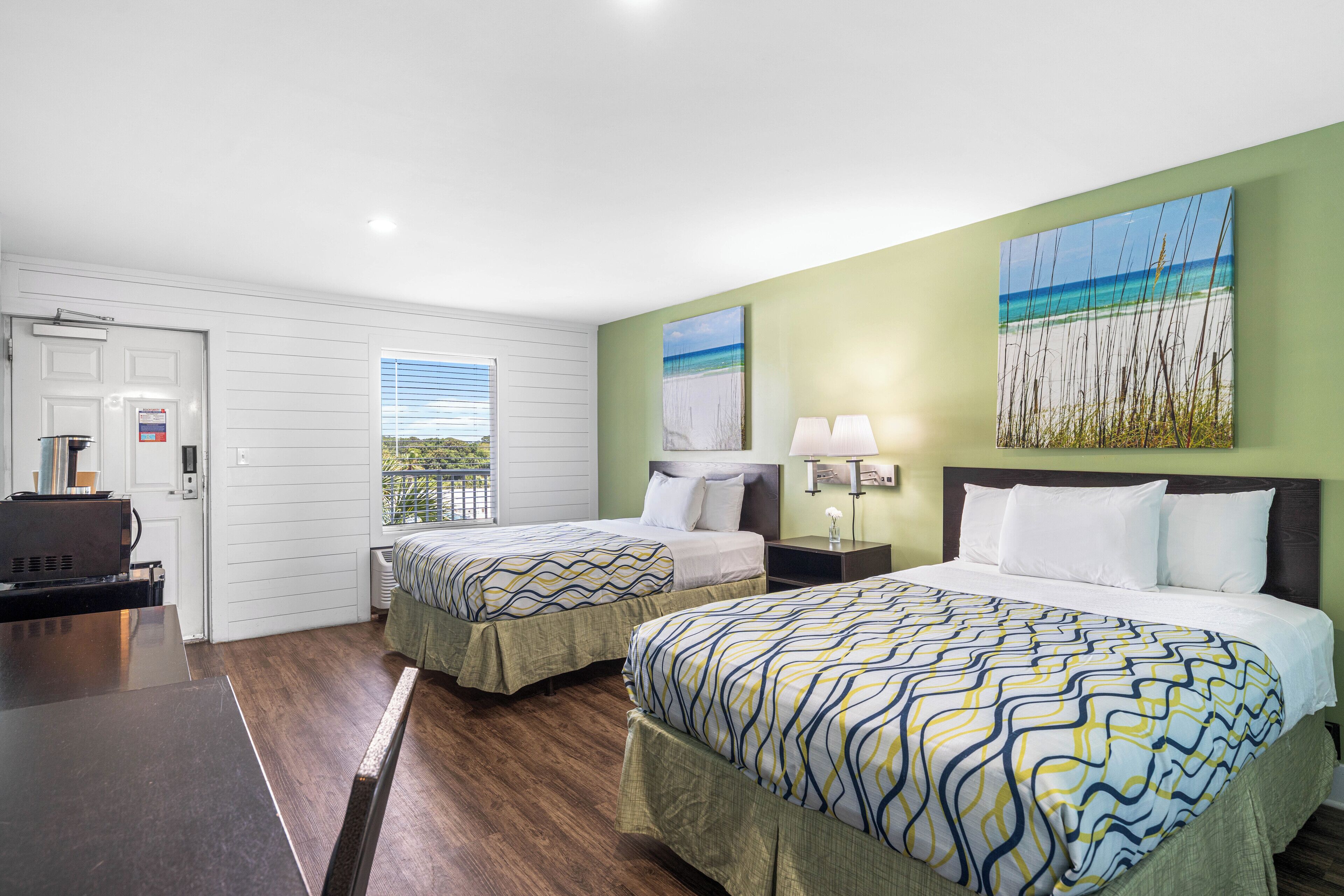 A hotel room with two beds, a desk, and a view of the beach.