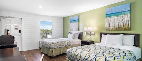 A hotel room with two beds, a desk, and a view of the beach.