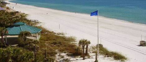 A beach with a flag, a covered structure, and a clear view of the ocean.