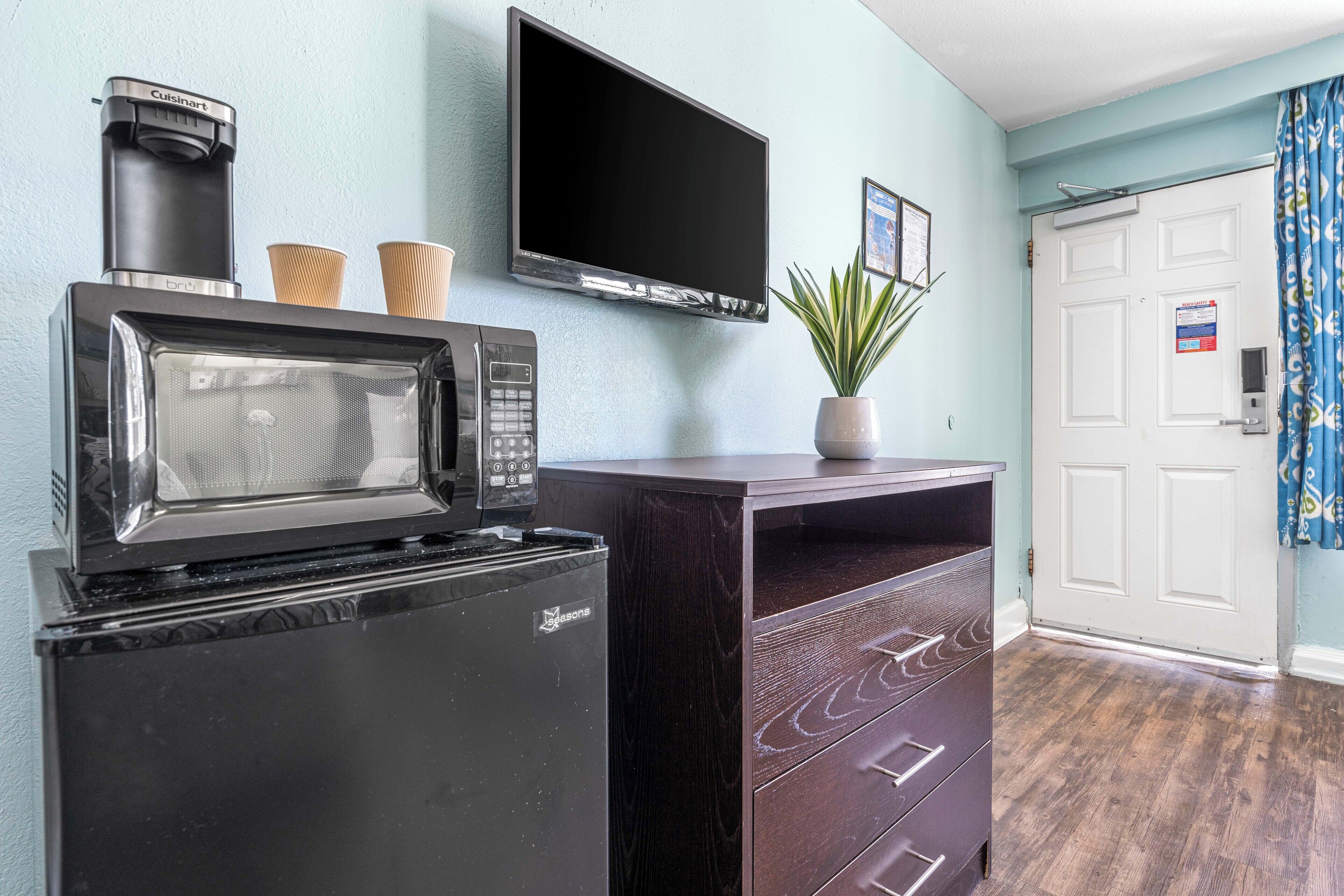 A compact kitchenette with a microwave, coffee maker, and toaster. A flat-screen TV is mounted on the wall above the counter.