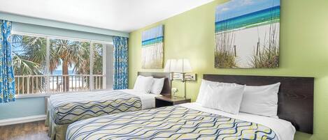 Habitación de hotel con dos camas, una ventana que ofrece vistas a palmeras y la playa, y una obra de arte que representa una escena costera.