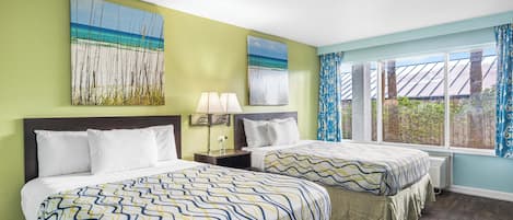 A hotel room with two beds, a large window with a view of the outdoors, and artwork on the walls.