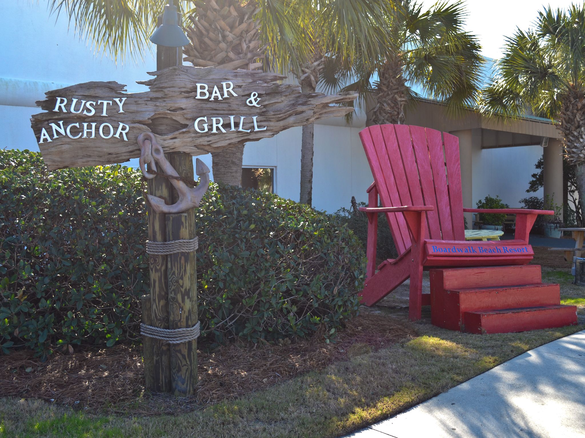 Ein hölzernes Wegweiser mit der Beschriftung 'Rusty Anchor Bar & Grill' und 'Boardwalk Beach Resort'.
