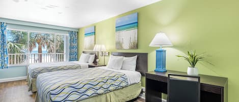 Habitación de hotel con dos camas, un escritorio, una silla, una lámpara y vistas a palmeras y al océano.