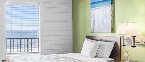 A hotel room with a bed, a nightstand with a lamp, a painting on the wall, and a window with blinds.