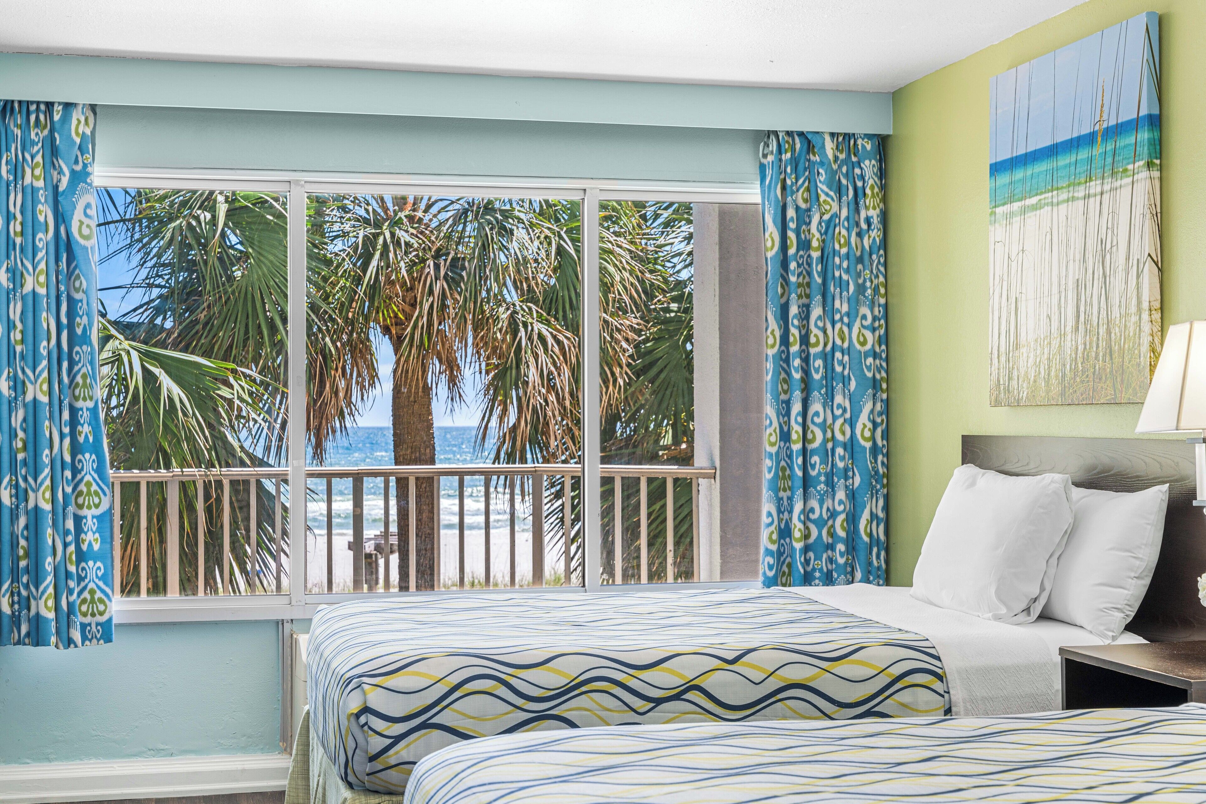 A hotel room with a large window overlooking palm trees and a beach.