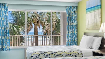 Habitación de hotel con un amplio ventanal que da a palmeras y una playa.
