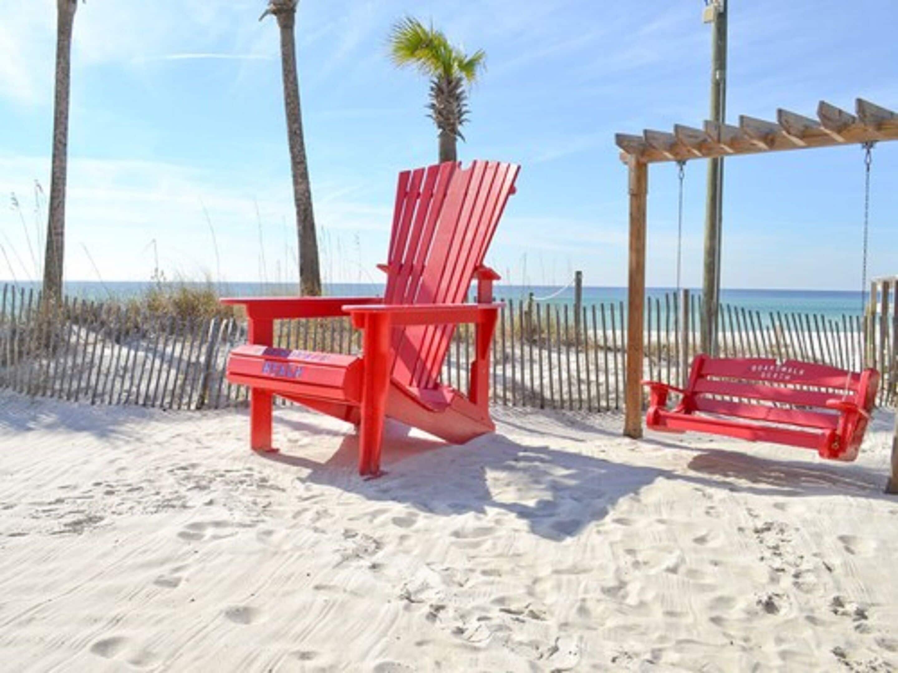 Escena de playa con dos sillas Adirondack rojas y un columpio de madera.