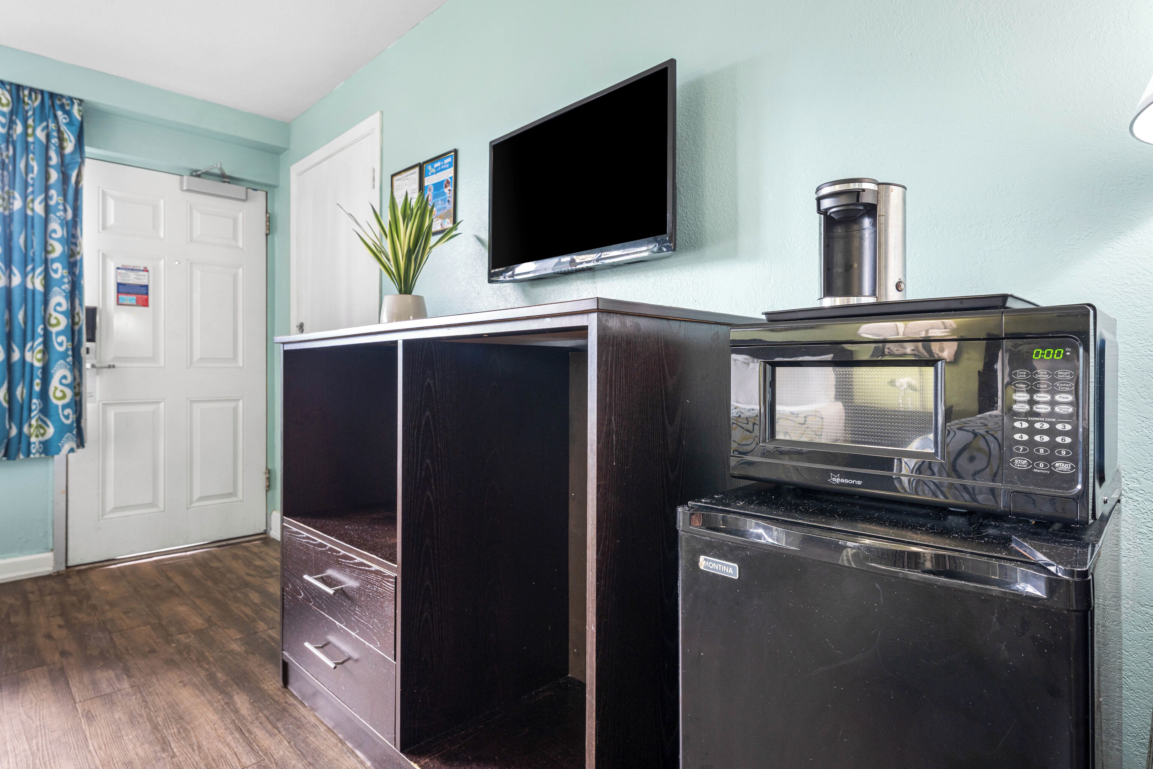A compact kitchen with a microwave and a coffee maker on a counter, a door with a sign, and a potted plant.