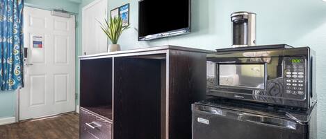 Una cocina compacta con microondas y cafetera sobre una encimera, una puerta con un letrero y una planta en maceta.