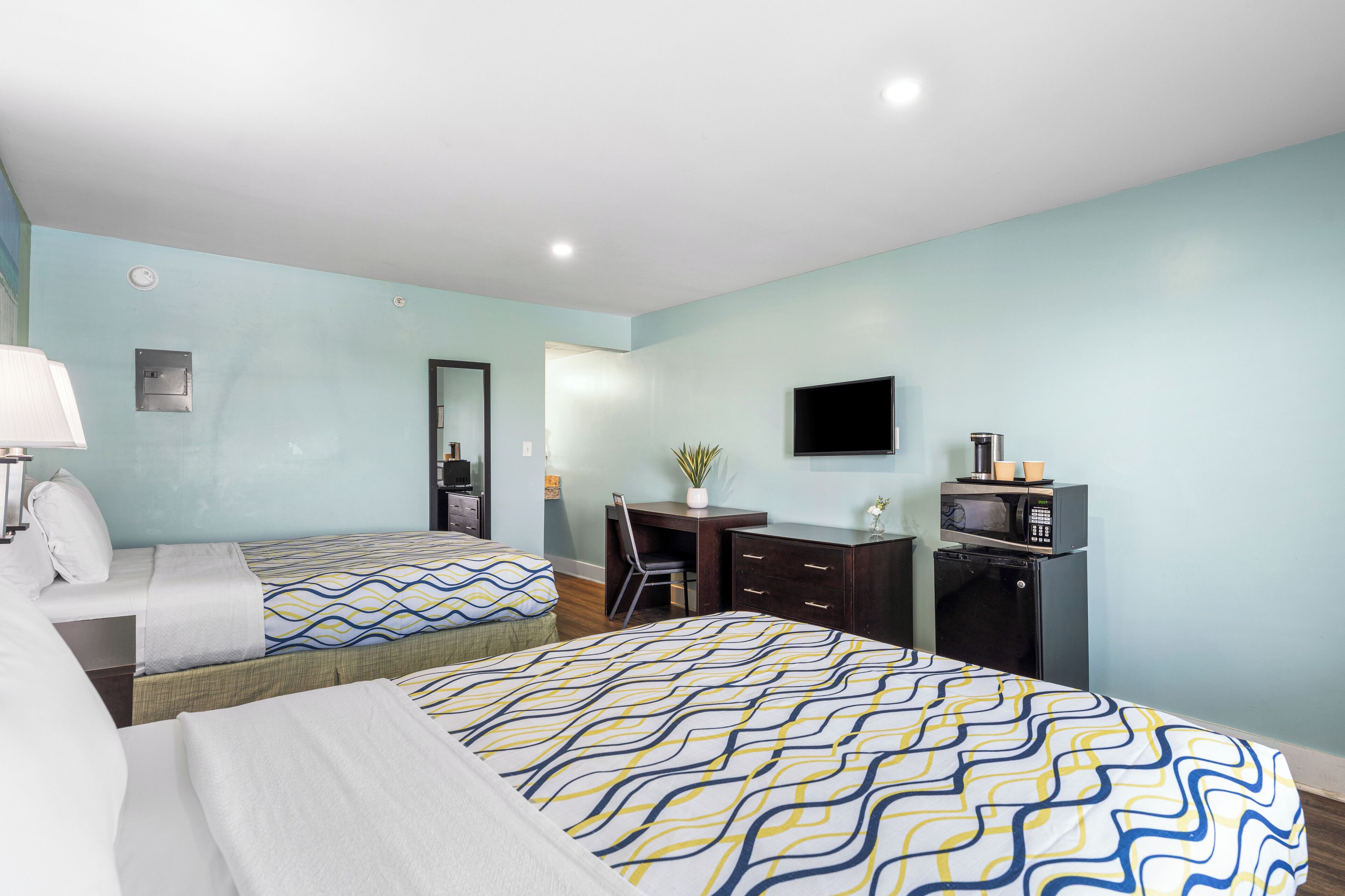 A hotel room with two beds, a desk, a TV, and a microwave.