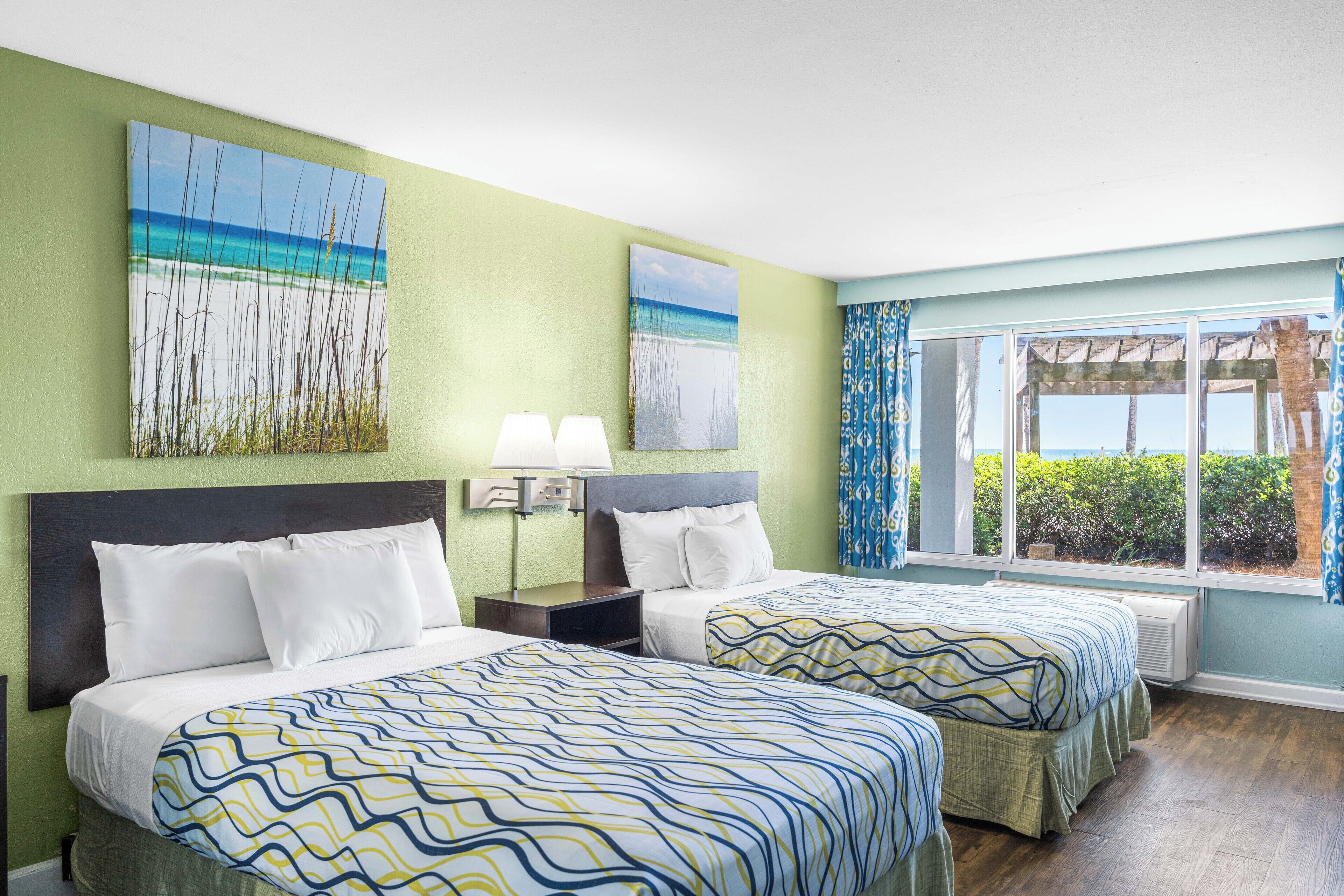 A hotel room with two beds, a large window with a view, and artwork on the walls.