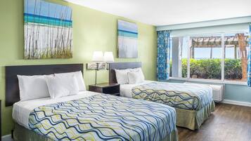 A hotel room with two beds, a large window with a view, and artwork on the walls.
