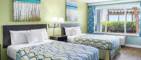 A hotel room with two beds, a large window with a view, and artwork on the walls.