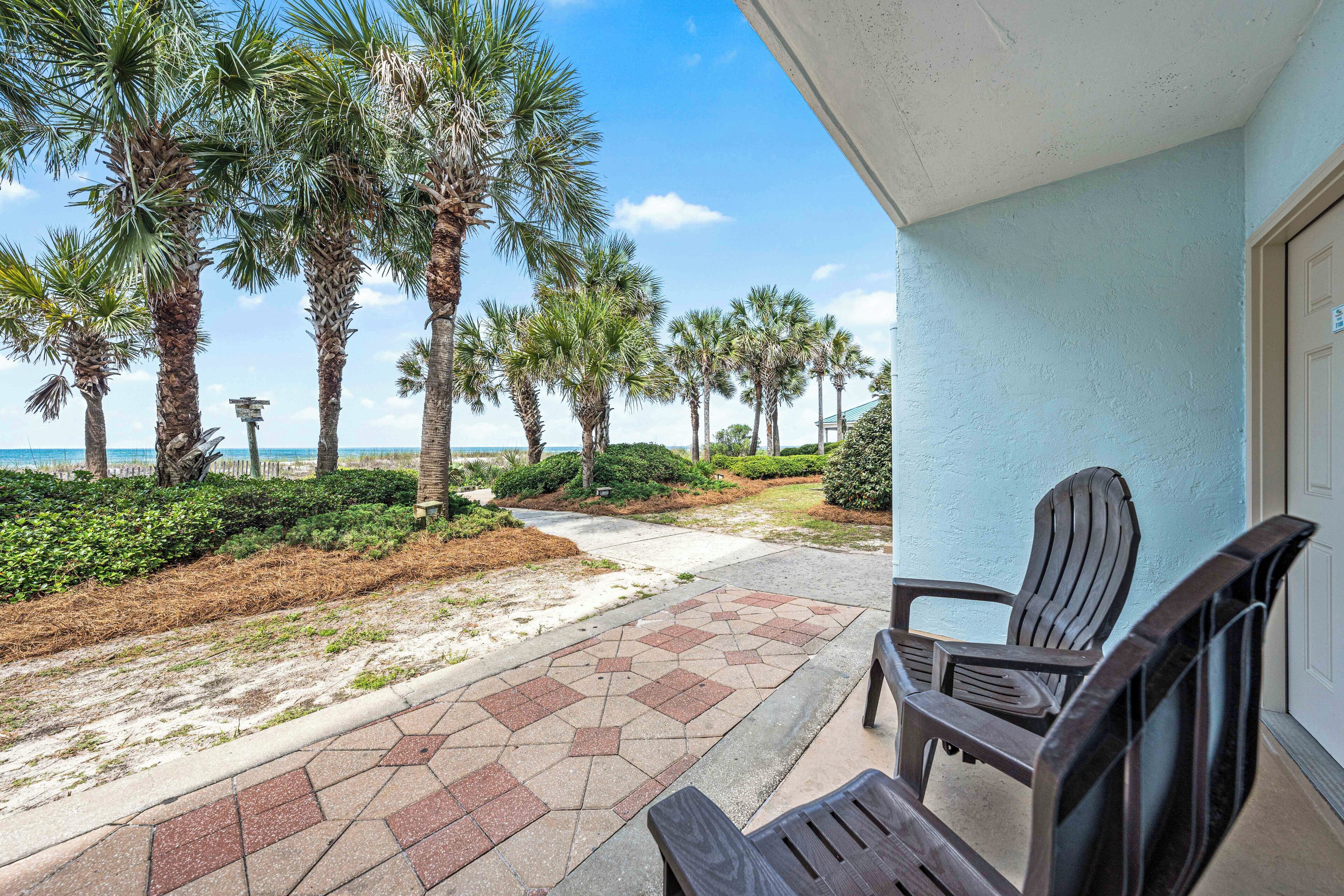 A beachside patio with chairs, palm trees, and a view of the ocean.