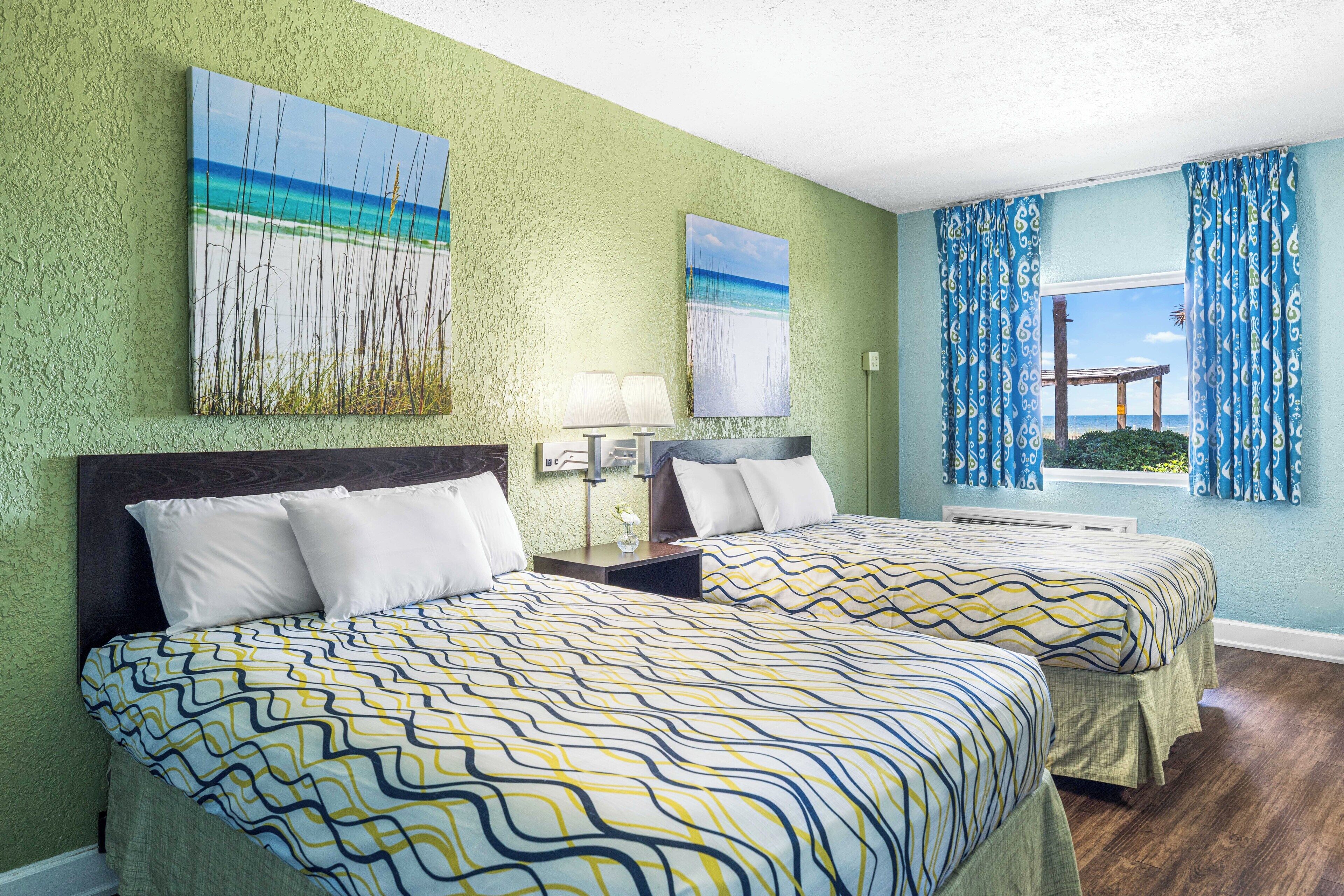 Une chambre d’hôtel avec deux lits, un mur décoré sur le thème de la plage et une fenêtre avec des rideaux.