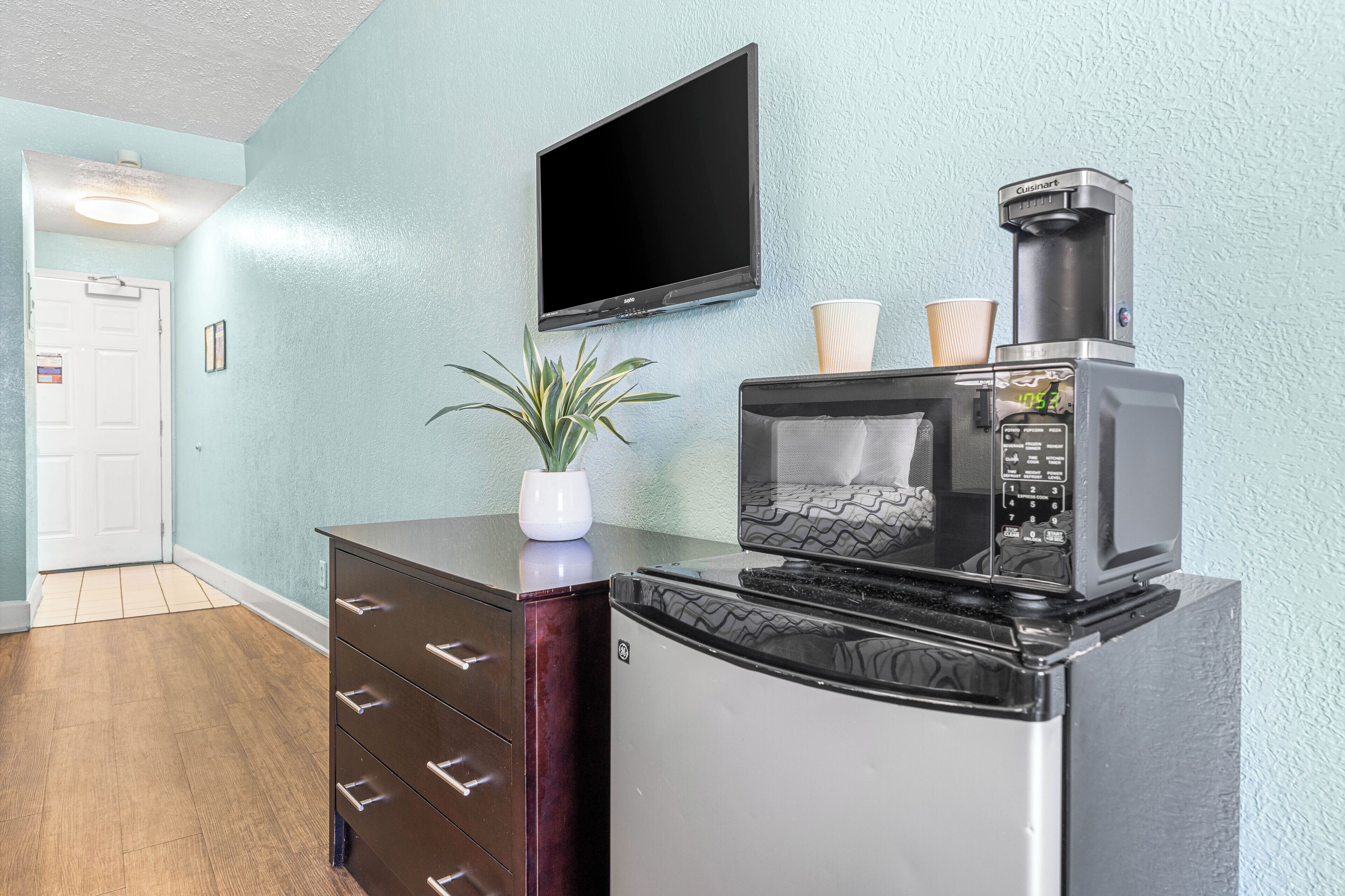 Una kitchenette compacta con microondas, cafetera y una pequeña planta en maceta.