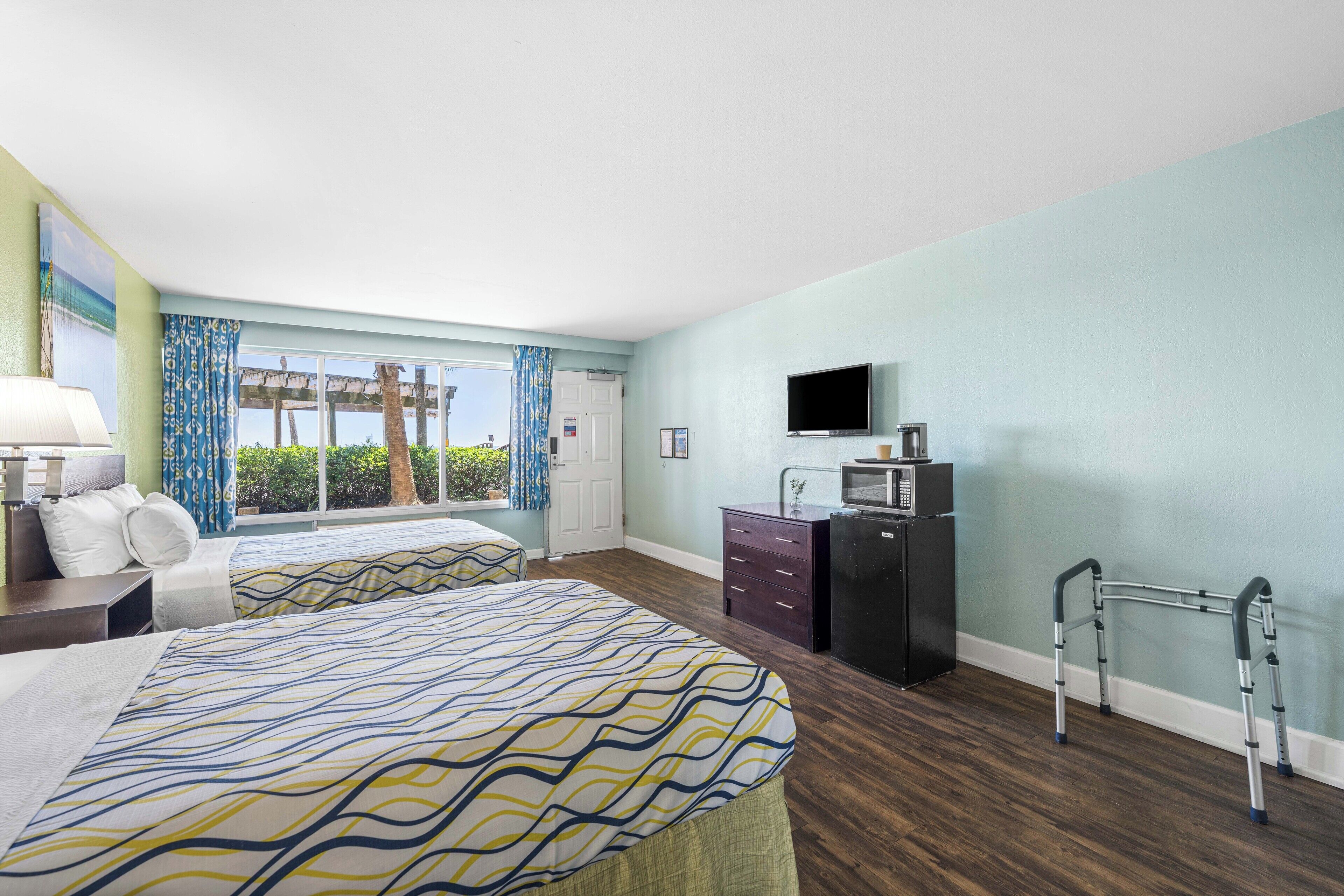 Habitación de hotel con dos camas, televisión, escritorio y ventana con cortinas.
