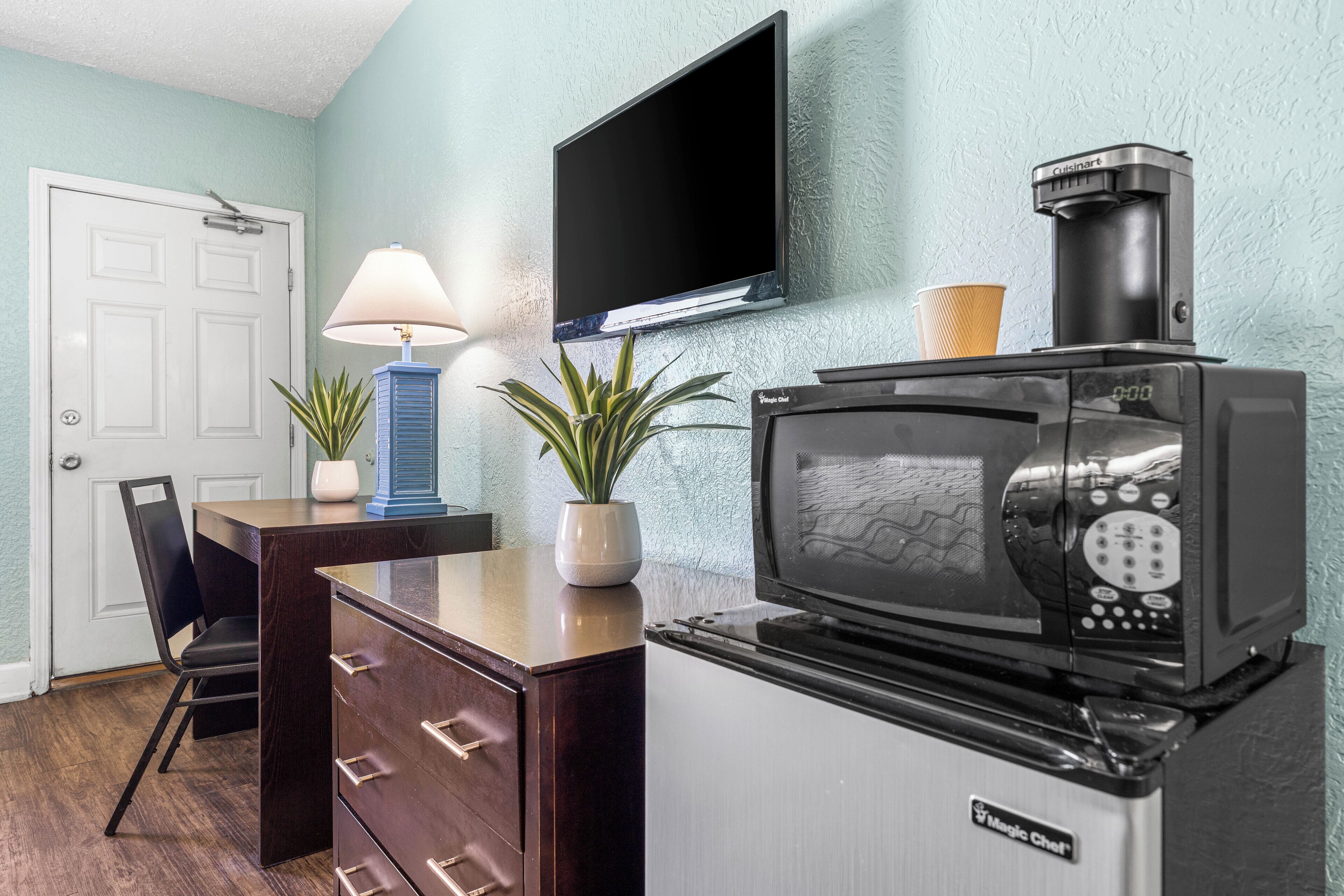 Uma cozinha compacta com micro-ondas, cafeteira e uma TV de tela plana na parede.