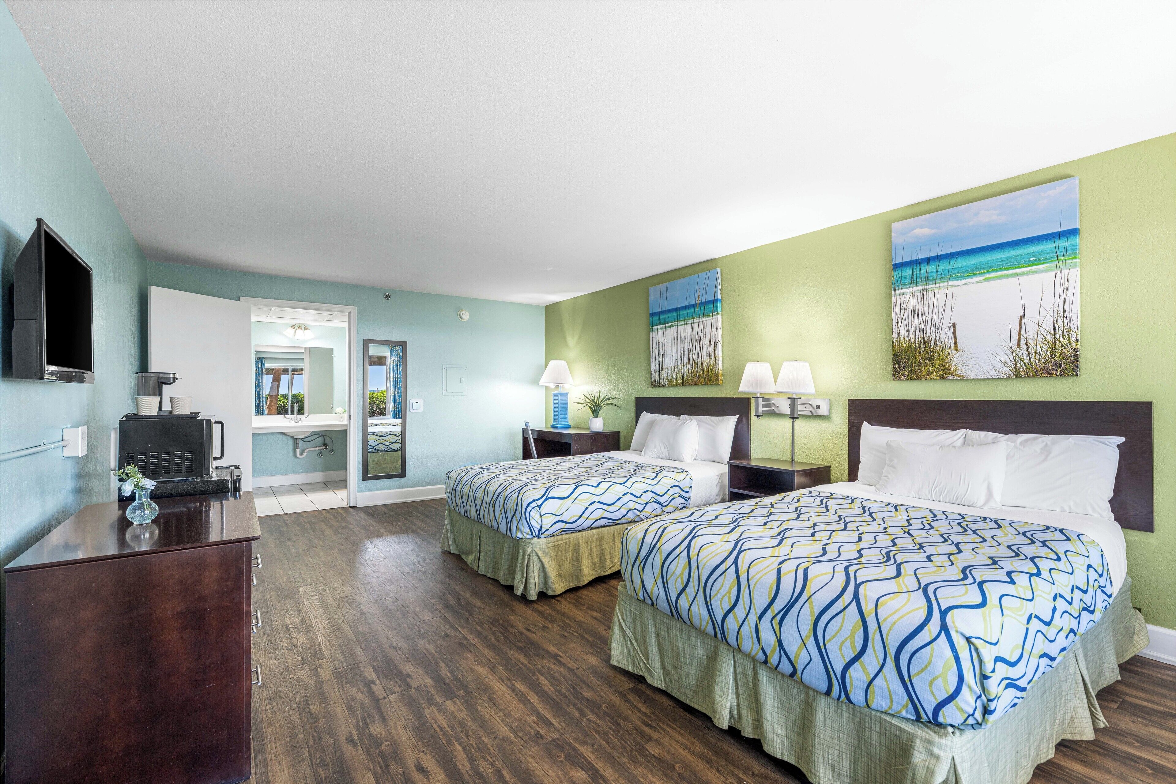 A hotel room with two beds, a desk, a TV, and artwork on the walls.