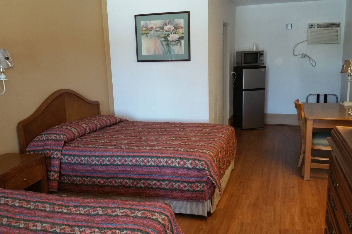 Habitación de hotel con dos camas, un escritorio, refrigerador, microondas y televisor.
