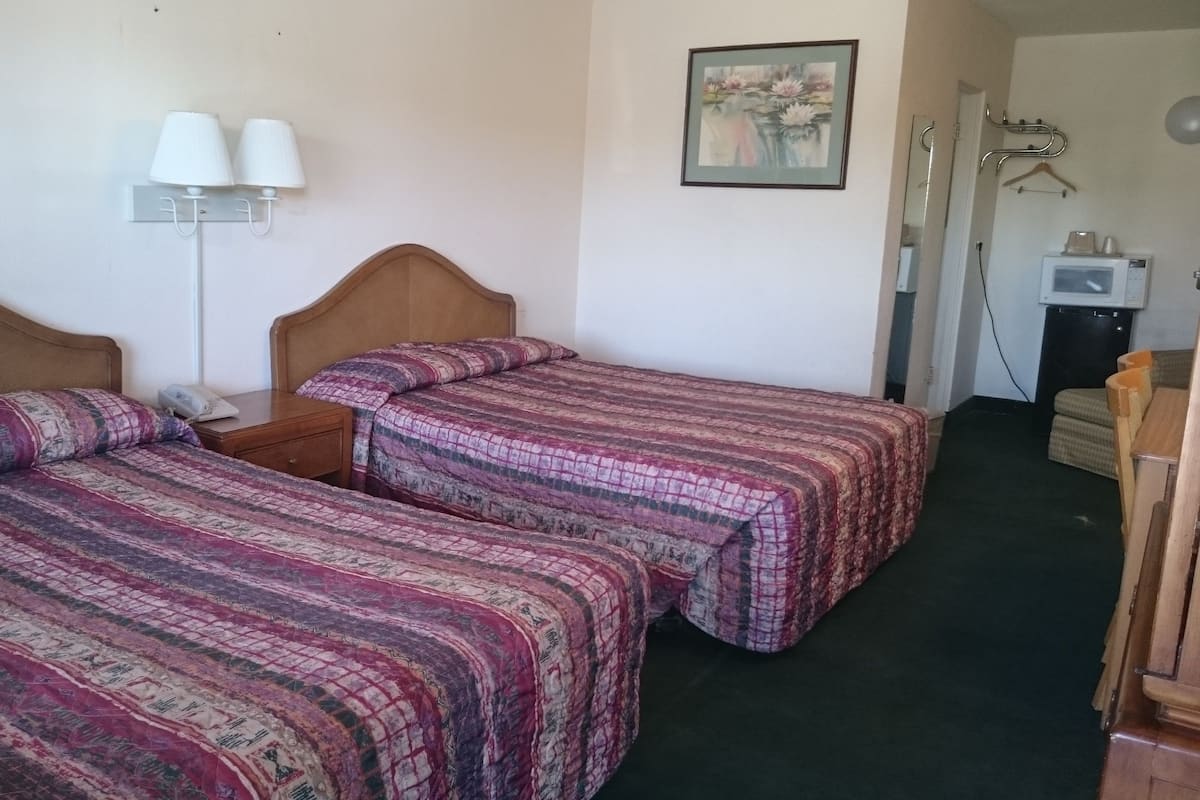 Dos camas individuales con ropa de cama estampada, una mesita de noche con lámpara, un cuadro en la pared y un microondas en una esquina.